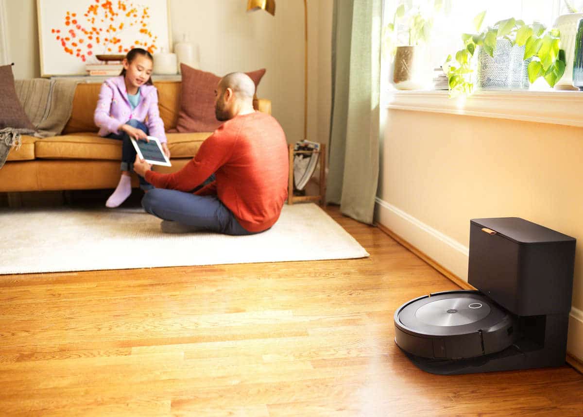 Picture of iRobot Roomba in a room, with a dad and daughter sitting near a couch nearby.