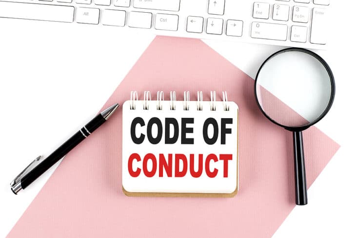 A notebook with the words "code of conduct" and a magnifying glass and pen